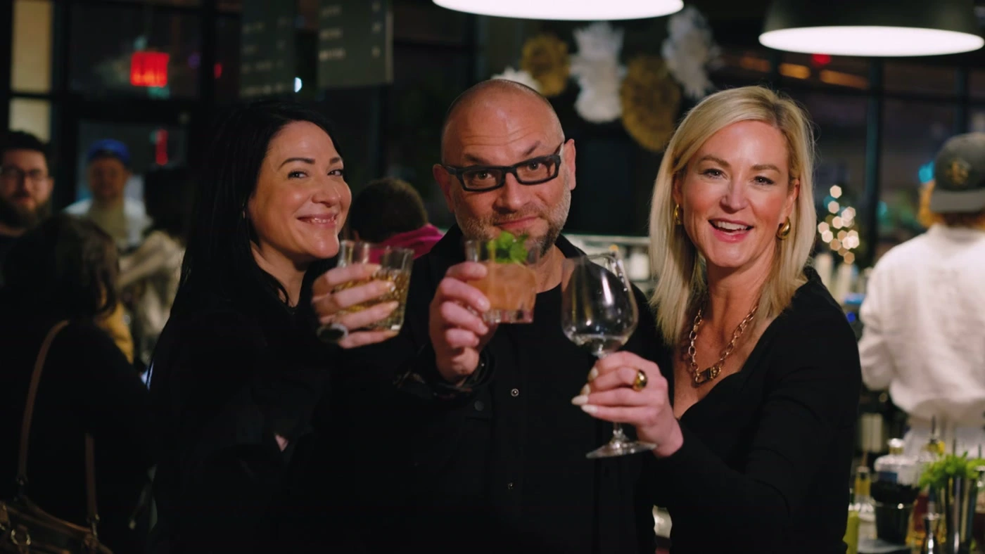 Three guests raising a toast to camera at a lively evening event